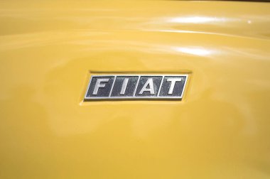 Larnaca, Cyprus- 12 Mayıs 2024: klasik sarı bir arabanın üzerinde parlayan krom Fiat logosu, otomotiv tarihinin ve zamansız tasarım zarafetinin özünü yakalıyor.
