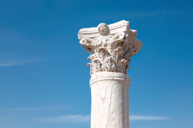 Kıbrıs 'taki Kourion arkeoloji sahasında, açık mavi gökyüzüne karşı yükselen kısmen korunmuş korint sütunu, antik mimarinin bir kanıtı.