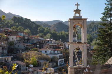 Resimli beyaz çan kulesi, Kıbrıs 'ın sakin Troodos dağlarına kurulmuş Platanistasa köyündeki geleneksel evlerin üzerinde yükseliyor. Lefkoşe Bölgesi