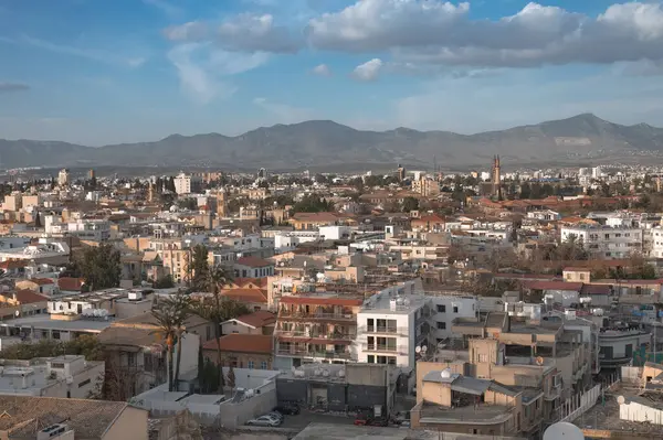 Kıbrıs 'ın başkenti Lefkoşe' nin panoramik manzarası, sıcak güneş ışığıyla yıkanmış, görkemli bir dağ zeminine karşı geleneksel mimarisini sergiliyor