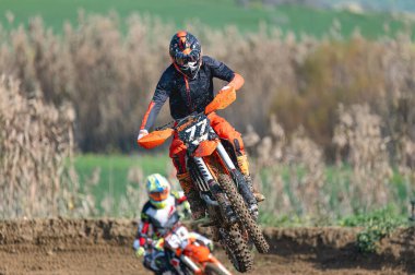 Motokros binicisi yoğun bir yarış sırasında havada süzülüyor. Olağanüstü bir yetenek ve kusursuz kontrol gösteriyor.