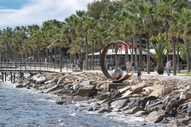 Limasol, Kıbrıs - 02 Ocak 2024: Limasol gezinti alanında gezinen turistler, Akdeniz manzarası ve modern bir heykelin keyfini çıkarıyorlar