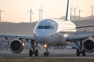 Larnaca, Kıbrıs - 24 Mayıs 2024: Arka planda rüzgar türbinleriyle havaalanında taksicilik yapan uçak, sürdürülebilir hava taşımacılığı ve yenilenebilir enerji gösteriyor