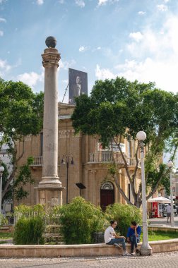 Lefkoşe, Kıbrıs - 31 Mayıs 2025: Atatürk Meydanı 'nda dikilen Venedik Sütunu, insanların ön planda dinlendiği ve arka planda Mustafa Kemal Atatürk' ün sancağı bulunan bir bina