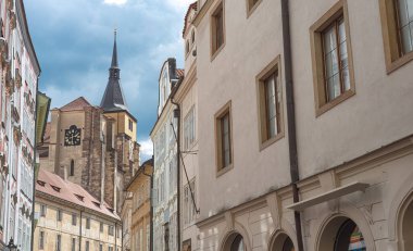 Husova caddesinde, bulutlu bir gökyüzünün altında kilise saat kulesi olan tarihi binalar.