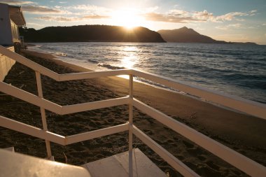 Wooden steps down to beach with waves and sand and island in the sunset.
