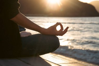 Gün batımında plajda yoga pozu veren bir kadın. Farkındalık ve zihinsel sağlık konsepti.