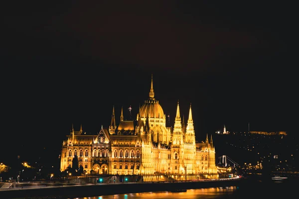 Illuminated Budapest parliament building at night with dark sky and reflection in Danube river.