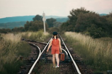 Demiryollarında eski bavullu küçük bir kızın Retro tarzı fotoğrafı.