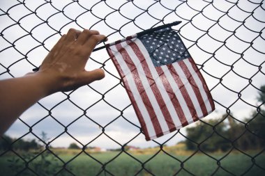 Close up of a American Flag in hand attached to a chain link fence. American immigration and United States refugee crisis concept clipart