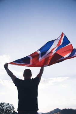 The flag of England waving in the hands of a man against the blue sky. View from the back. Great Britain, victory and success