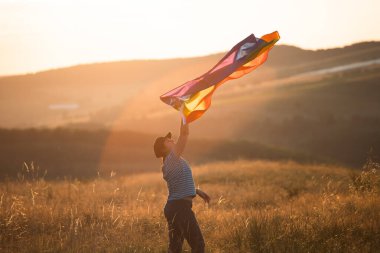 Sihirli günbatımında elinde Gay Gökkuşağı Bayrağı tutan bir kadın. Aynı cinsiyet çiftleri için mutluluk, özgürlük ve aşk kavramı