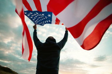 Man holding american USA flag in the sunset. Independence Day or traveling in America concept.