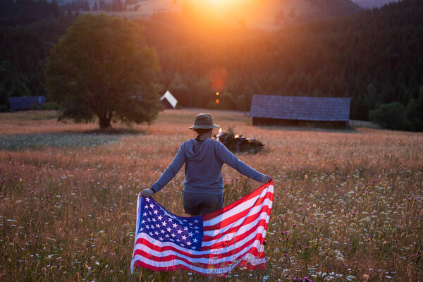 Young woman holding american USA flag in the sunset. Independence Day or traveling in America concept. 