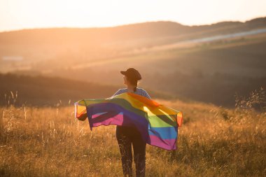 Woman holding a Gay Rainbow Flag in magic sunset. Happiness, freedom and love concept for same sex couples