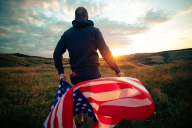 Gün batımında Amerikan bayrağı tutan adam. Bağımsızlık Günü ya da Amerika 'da seyahat.