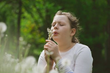 Küçük beyaz kız bahar bahçesinde karahindiba üflüyor..