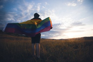 Elinde Gay Gökkuşağı Bayrağı tutan genç bir adam. Aynı cinsiyet çiftleri için mutluluk, özgürlük ve aşk kavramı