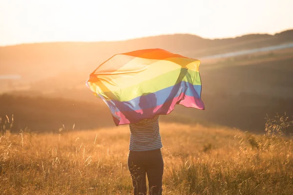 Woman holding a Gay Rainbow Flag in magic sunset. Happiness, freedom and love concept for same sex couples