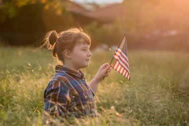 Gün batımı tarlasında Amerikan bayrağı taşıyan şirin bir kız çocuğu. ABD 4 Temmuz 'u kutladı.