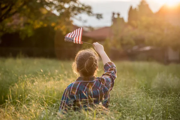 Gün batımı tarlasında Amerikan bayrağı taşıyan şirin bir kız çocuğu. ABD 4 Temmuz 'u kutladı.
