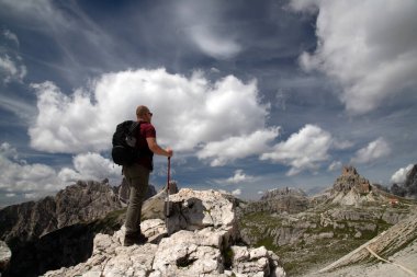 Erkek yürüyüşçü, İtalya 'nın Dolomites kentindeki Tre Cime di Lavaredo Ulusal Parkı' ndaki etkileyici zirvelerin çarpıcı güzelliğine hayran kalarak ayakta duruyor..