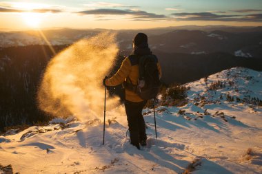 Karda yürüyen bir adam sihirli günbatımıyla kaplı bir dağda. Doğadaki aktif insanlar, macera konsepti.