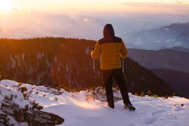 Karda yürüyen bir adam sihirli günbatımıyla kaplı bir dağda. Doğadaki aktif insanlar, macera konsepti.