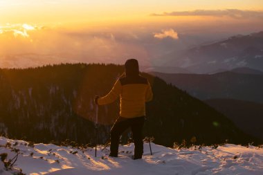Karda yürüyen bir adam sihirli günbatımıyla kaplı bir dağda. Doğadaki aktif insanlar, macera konsepti.