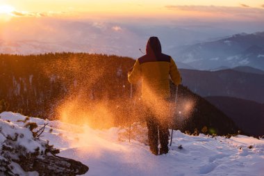 Karda yürüyen bir adam sihirli günbatımıyla kaplı bir dağda. Doğadaki aktif insanlar, macera konsepti.