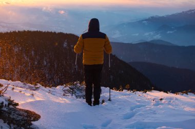 Karda yürüyen bir adam sihirli günbatımıyla kaplı bir dağda. Doğadaki aktif insanlar, macera konsepti.