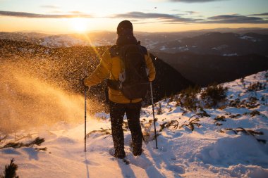Karda yürüyen bir adam sihirli günbatımıyla kaplı bir dağda. Doğadaki aktif insanlar, macera konsepti.