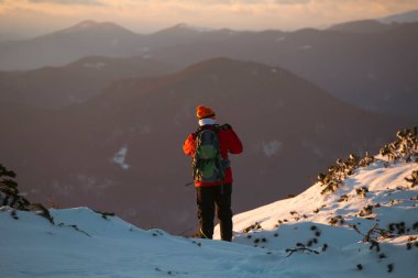 Karda yürüyen bir adam sihirli günbatımıyla kaplı bir dağda. Doğadaki aktif insanlar, macera konsepti.