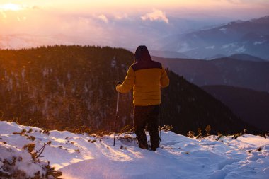 Karda yürüyen bir adam sihirli günbatımıyla kaplı bir dağda. Doğadaki aktif insanlar, macera konsepti.
