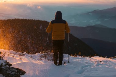 Karda yürüyen bir adam sihirli günbatımıyla kaplı bir dağda. Doğadaki aktif insanlar, macera konsepti.