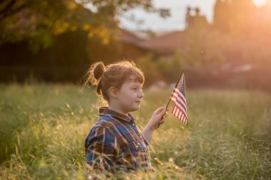 Gün batımı tarlasında Amerikan bayrağı taşıyan şirin bir kız çocuğu. ABD 4 Temmuz 'u kutladı.