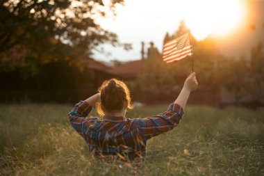 Gün batımı tarlasında Amerikan bayrağı taşıyan şirin bir kız çocuğu. ABD 4 Temmuz 'u kutladı.