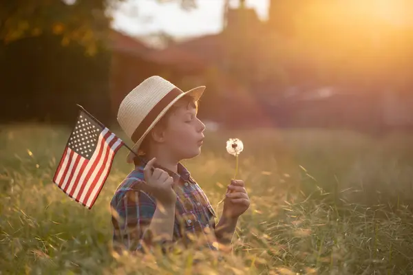 日没のフィールドにアメリカの旗を持つかわいい子供の女の子 アメリカは7月4日を祝う ストックフォト