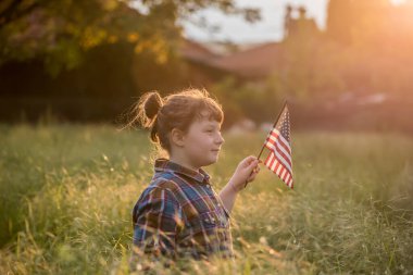 Gün batımı tarlasında Amerikan bayrağı taşıyan şirin bir kız çocuğu. ABD 4 Temmuz 'u kutladı.