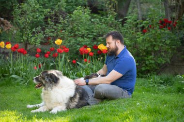 Yakışıklı adam bahar bahçesinde mutlu köpeğiyle oynuyor.