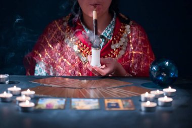 Falcı elinde tarot kartlarıyla yanan mumların yanındaki masada..