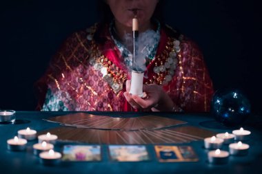 Falcı elinde tarot kartlarıyla yanan mumların yanındaki masada..