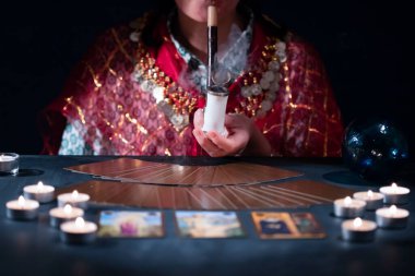 Falcı elinde tarot kartlarıyla yanan mumların yanındaki masada..