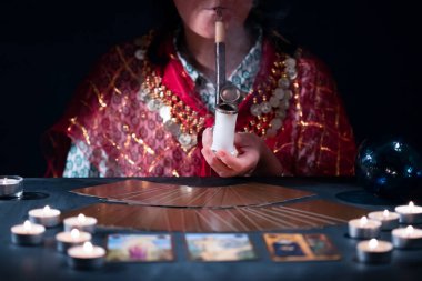 Falcı elinde tarot kartlarıyla yanan mumların yanındaki masada..