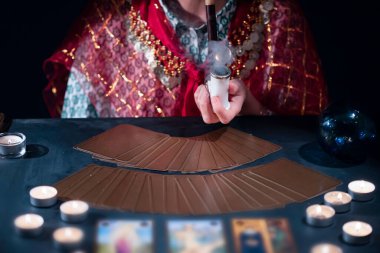 Falcı elinde tarot kartlarıyla yanan mumların yanındaki masada..