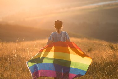 Woman holding a Gay Rainbow Flag in magic sunset. Happiness, freedom and love concept for same sex couples