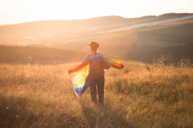 Sihirli günbatımında elinde Gay Gökkuşağı Bayrağı tutan bir kadın. Aynı cinsiyet çiftleri için mutluluk, özgürlük ve aşk kavramı