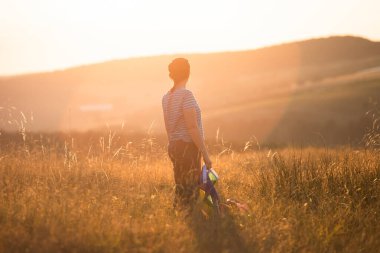 Sihirli günbatımında elinde Gay Gökkuşağı Bayrağı tutan bir kadın. Aynı cinsiyet çiftleri için mutluluk, özgürlük ve aşk kavramı