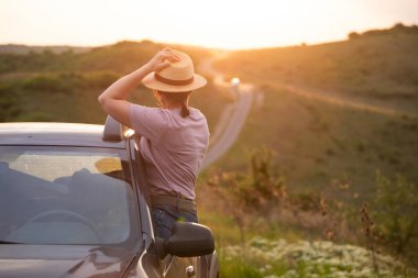 Arabasında yaz şapkası olan bir kadın yolda seyahat ediyor. Özgürlük, seyahat ve tatil yolculuğu konsept yaşam tarzı imajı