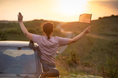 Gün batımında Amerikan bayrağı taşıyan bir kadın. Bağımsızlık Günü ya da Amerika 'da seyahat.